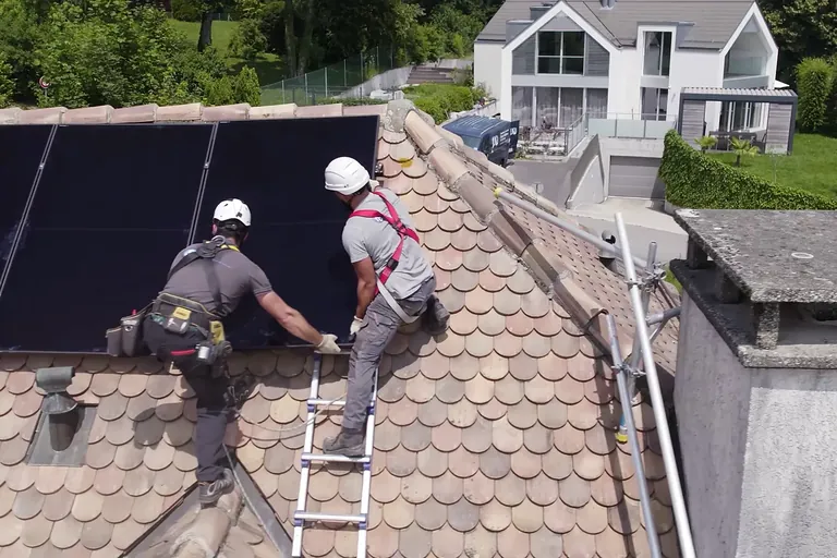 Deux techniciens posent des panneaux photovoltaïques sur une toiture en tuiles, Suisse romande